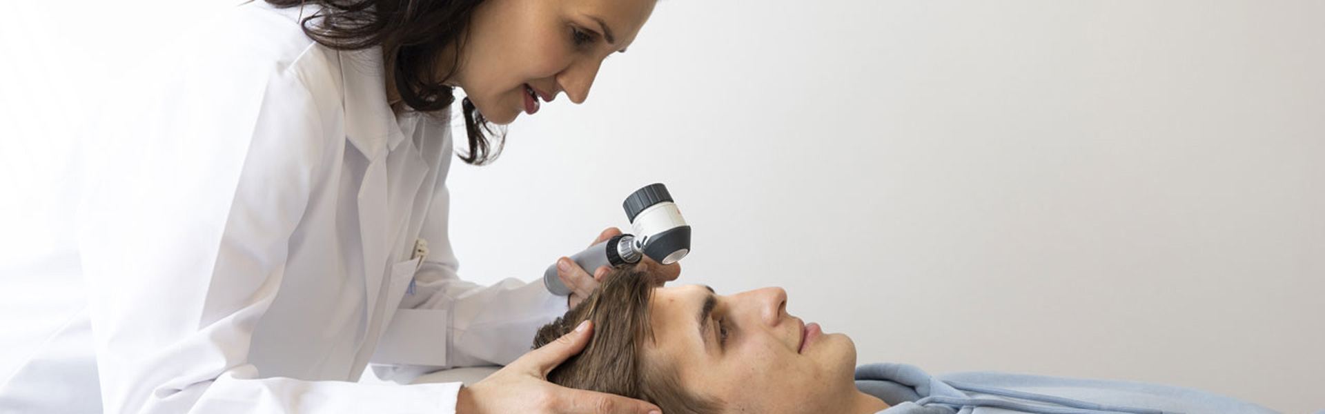 Dermatologinja z dermatoskopom pregleduje pacienta
